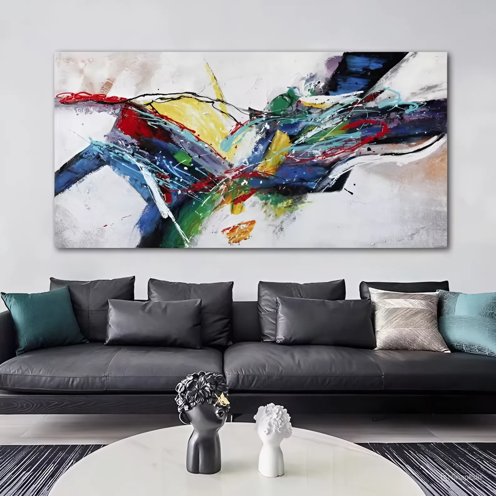 A modern living room with a sleek black leather sofa adorned with plush pillows in shades of green and grey. Above the sofa hangs a large, vibrant abstract wall art painting featuring a dynamic explosion of colors, including red, yellow, blue, green, and white, creating a striking focal point.